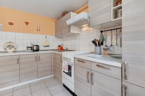 A modern kitchen with light wood cabinets, a white countertop, and a stainless steel range hood.