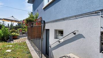 En boligbygning med en blå facade, et lille vindue med dekorativt gitter, gelænder og en potteplante med røde blomster.