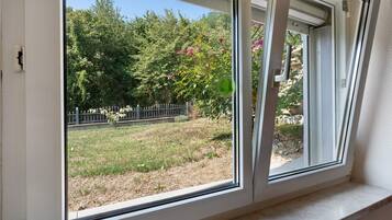 A window with a view of a garden, a metal fence, and a stone wall.