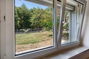 A window with a view of a garden, a metal fence, and a stone wall.