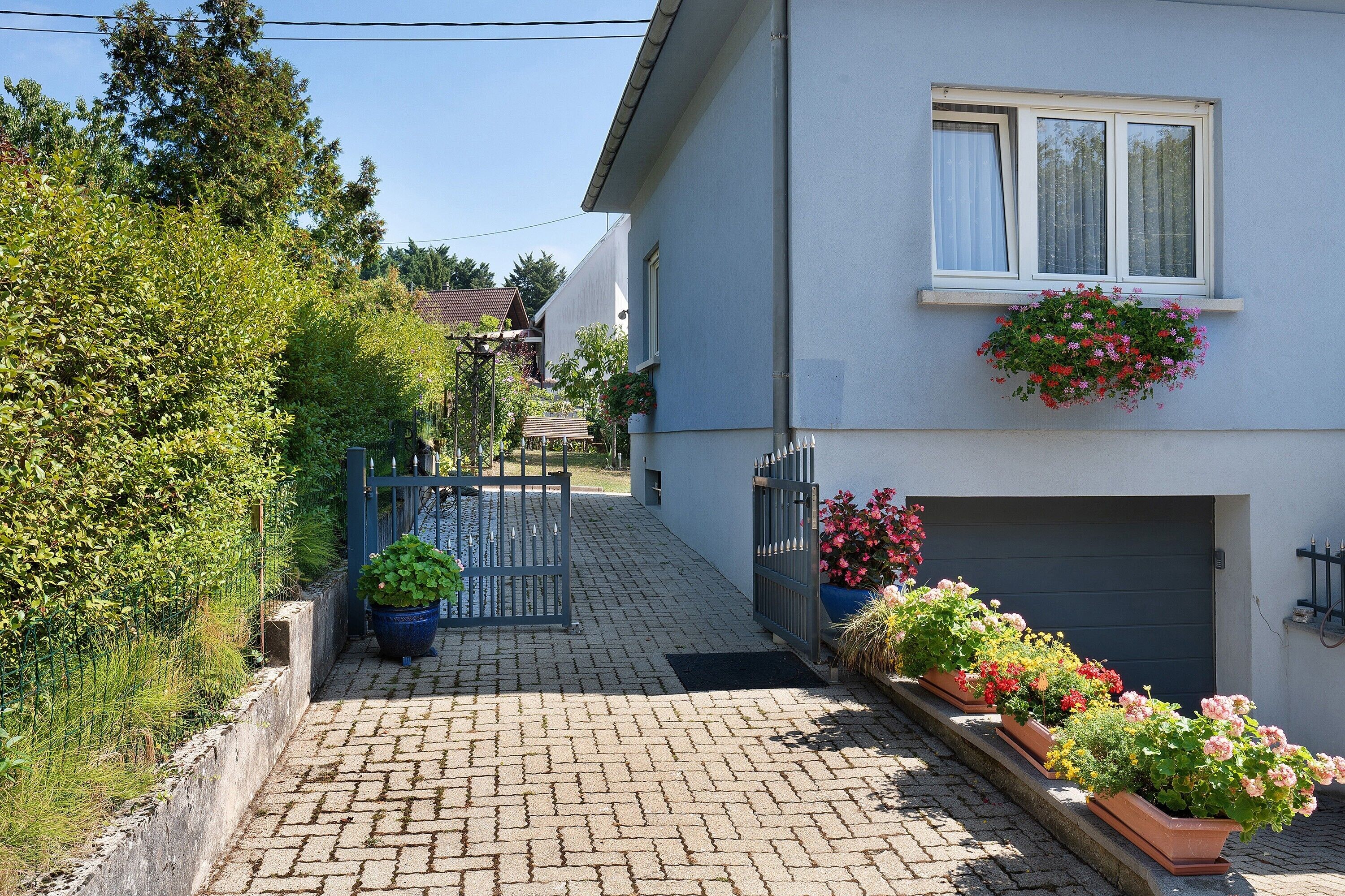 A residential street with a paved pathway, a metal gate, and a house with a garage door.