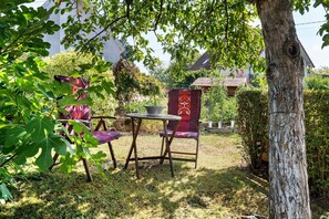 Un espacio de estar al aire libre con una mesa y sillas, rodeado de vegetación y un árbol.