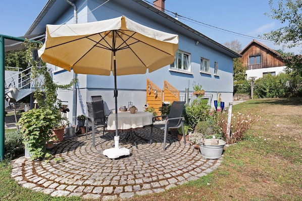 A patio with a table and chairs, a large umbrella, and potted plants.