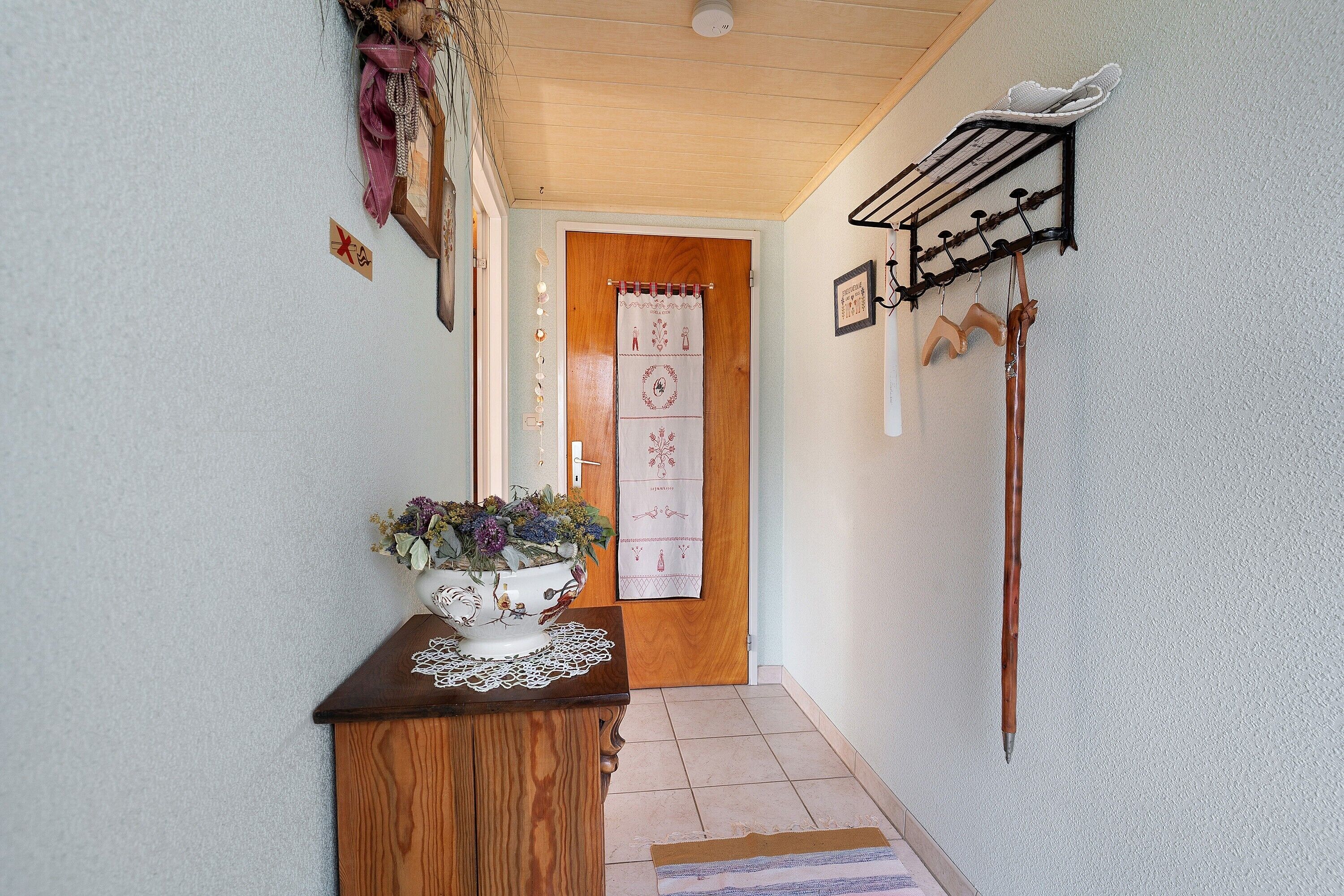 A hallway with a wooden door, a wall-mounted rack, and a decorative vase on a table.