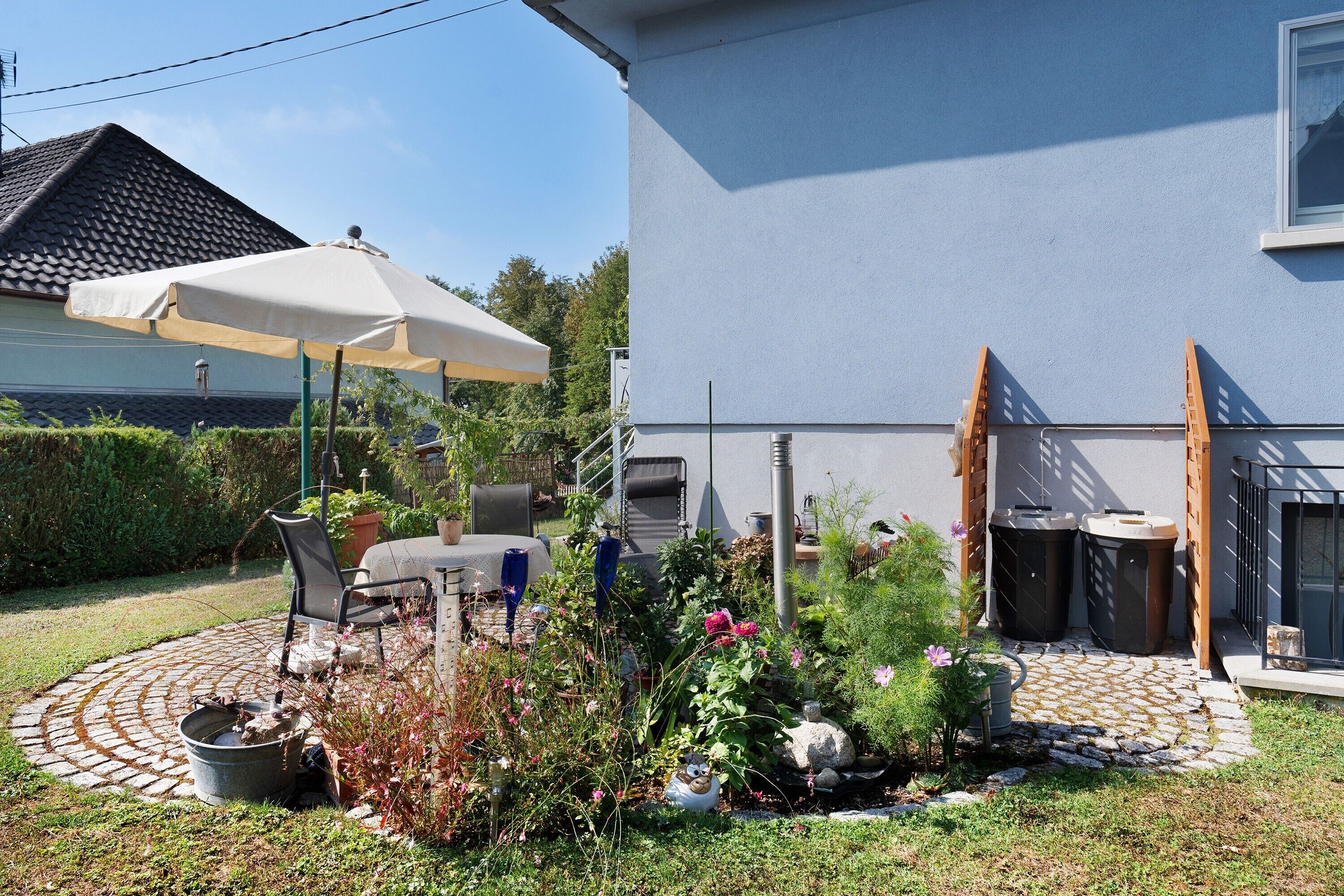 Une terrasse avec une table et des chaises, un pot de fleurs et un petit espace aménagé en jardin.