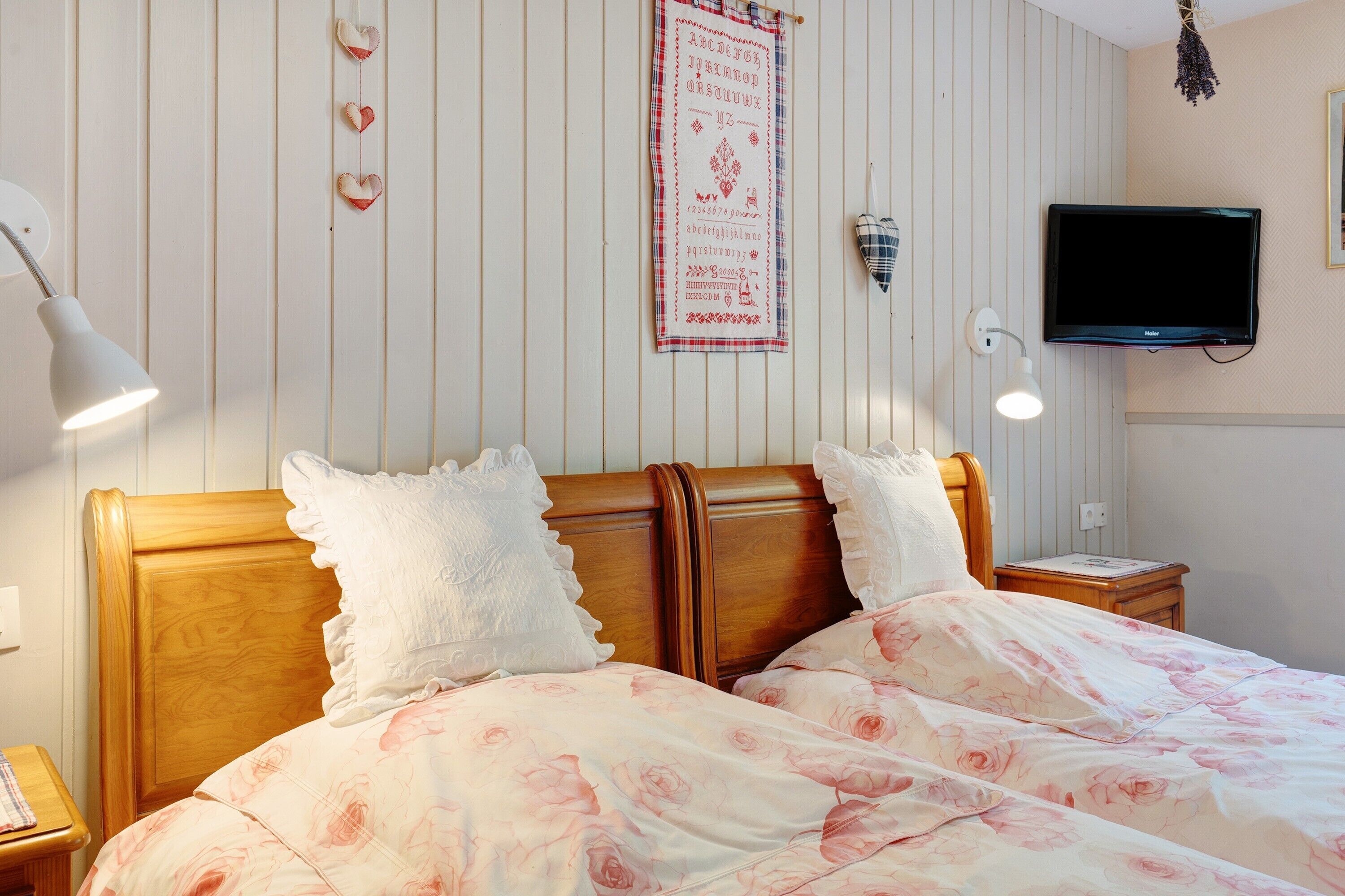 A bedroom with a wooden headboard, a bed with floral bedding, a wall-mounted TV, and a decorative heart garland.