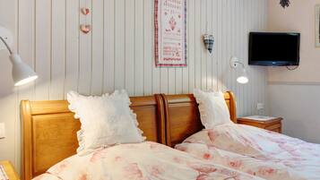 A bedroom with a wooden headboard, a bed with floral bedding, a wall-mounted TV, and a decorative heart garland.