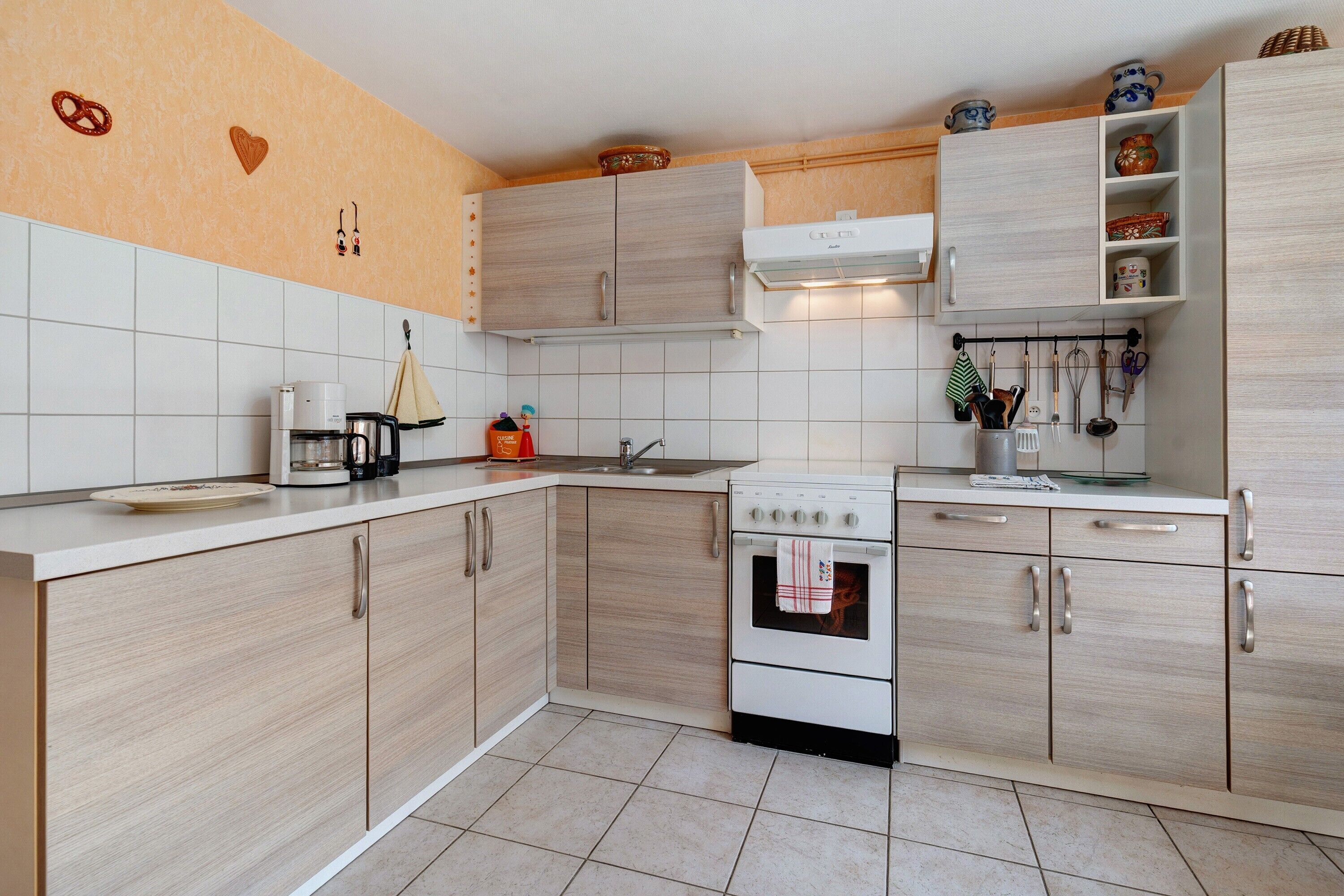 Une cuisine avec des meubles de couleur bois clair, une cuisinière blanche et une machine à café.