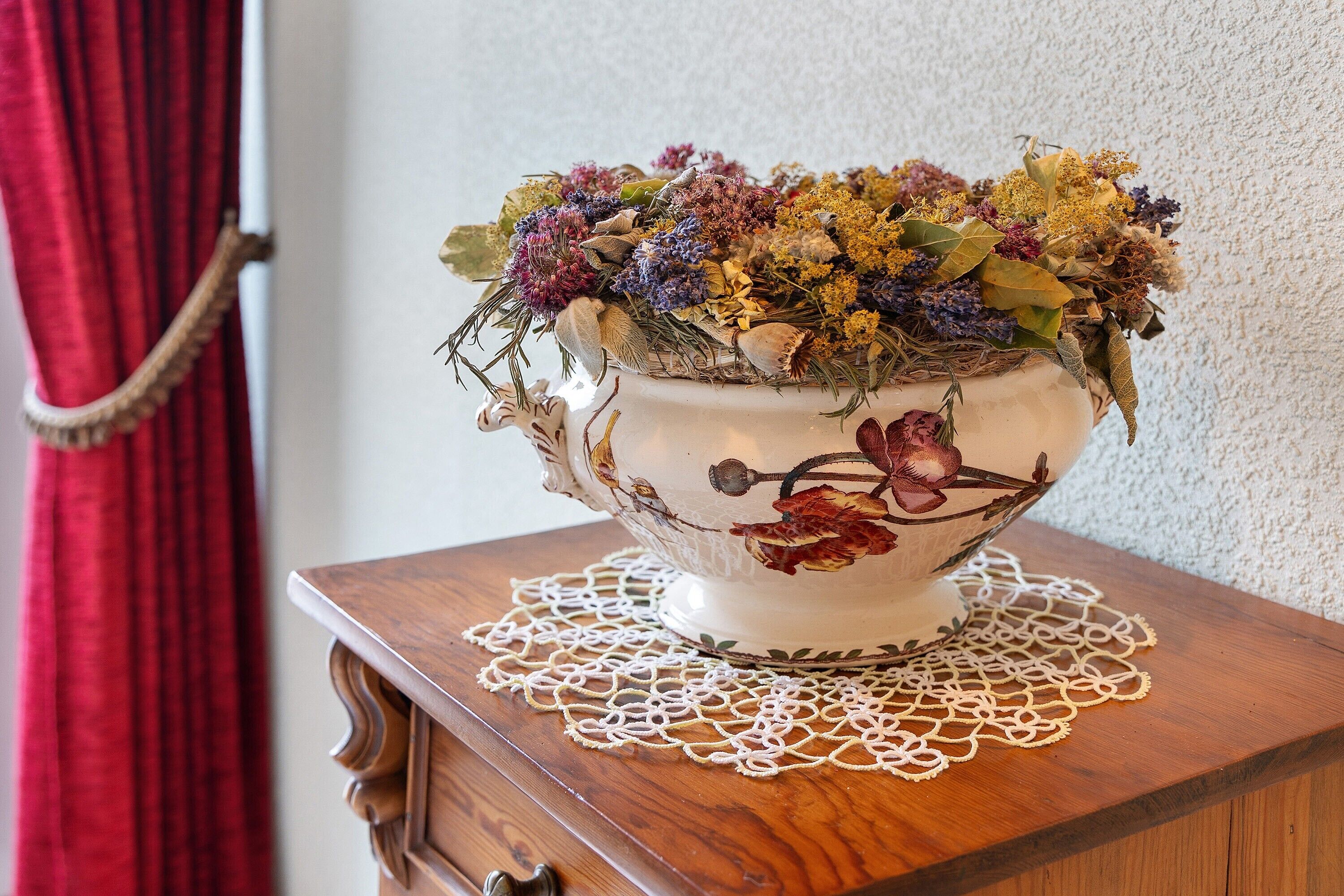A decorative bowl with dried flowers and leaves on a wooden table with a lace doily.