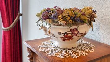 A decorative bowl with dried flowers and leaves on a wooden table with a lace doily.