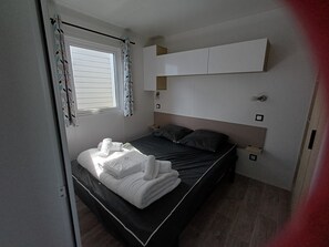 Un letto singolo con poggiatesta, una finestra con tende, un comodino e un armadietto a muro sopra il letto.