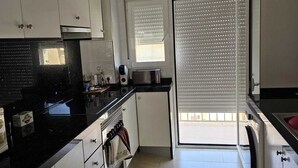 Una cocina con armarios blancos, encimera negra y suelo de baldosas.