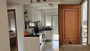 Un amplio espacio de sala con un sofá, una cocina al fondo y una puerta de madera.