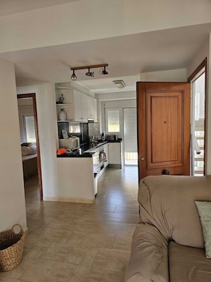 A spacious living area with a sofa, a kitchen in the background, and a wooden door. - Las Perlas Development, Las Marinas Highway (Denia)
