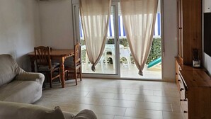 Una sala de estar con sofá, una mesa de comedor y sillas, un mueble de madera y un ventanal corredero que da a un área exterior.