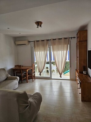 A living room with a sofa, a dining table, and chairs, a wooden cabinet, and a sliding glass door leading to an outdoor area. - Las Perlas Development, Las Marinas Highway (Denia)