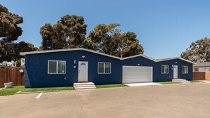 Ein eingeschossiges blaues Haus mit Garage, Eingangstür und kleinem Vorgarten.