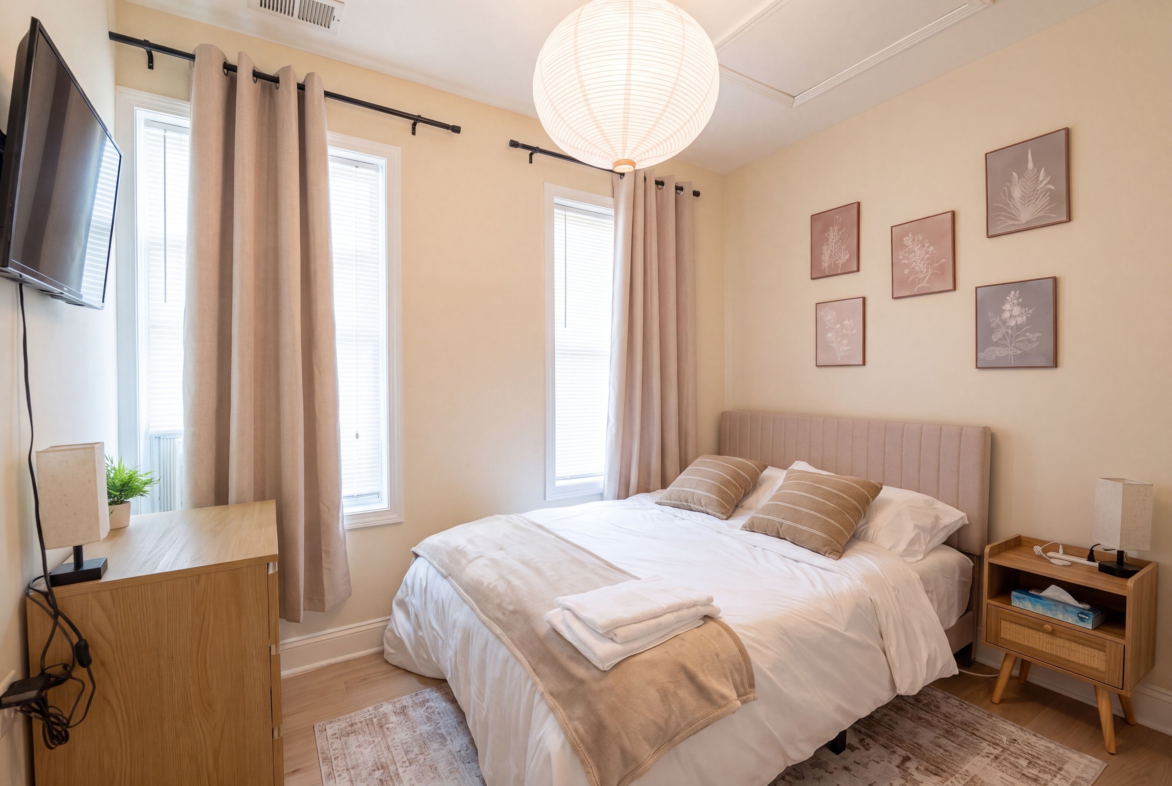 A bedroom with a bed, bedside tables, a TV, and artwork on the wall.