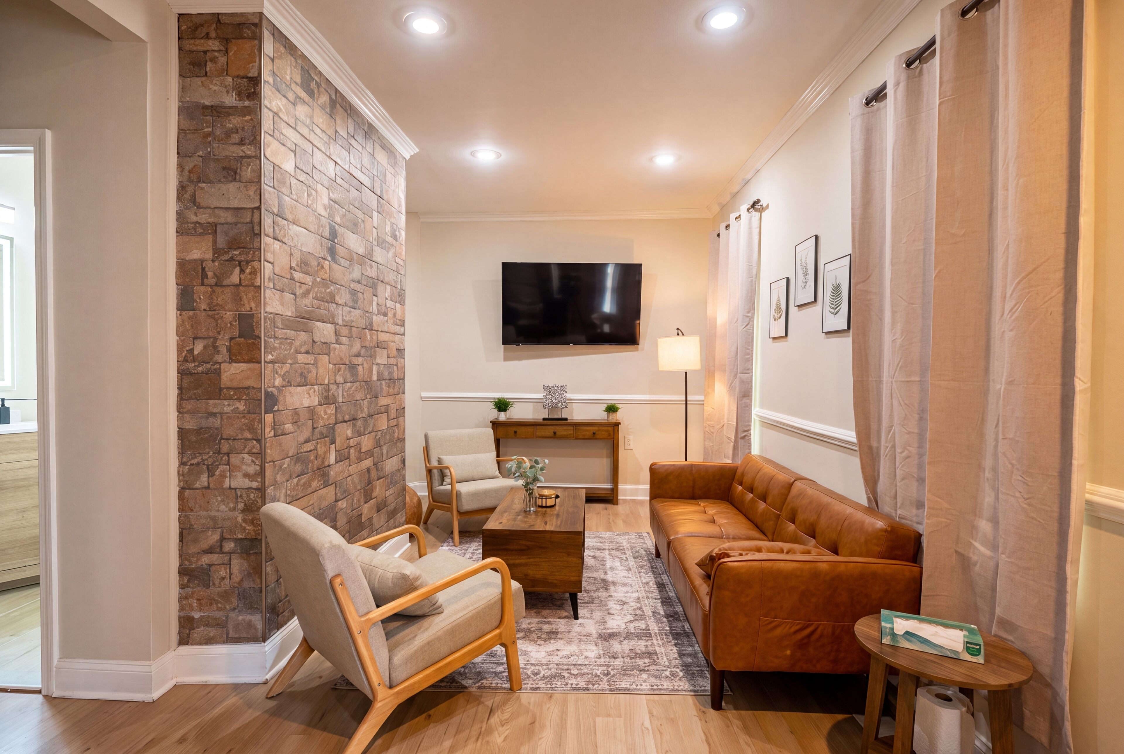 A living room with a stone accent wall, a flat-screen TV, a sofa, a chair, a coffee table, and a small side table.