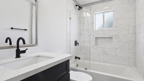 Ein modernes Badezimmer mit einem weißen Waschbecken, einem schwarzen Wasserhahn und einer Badewanne.