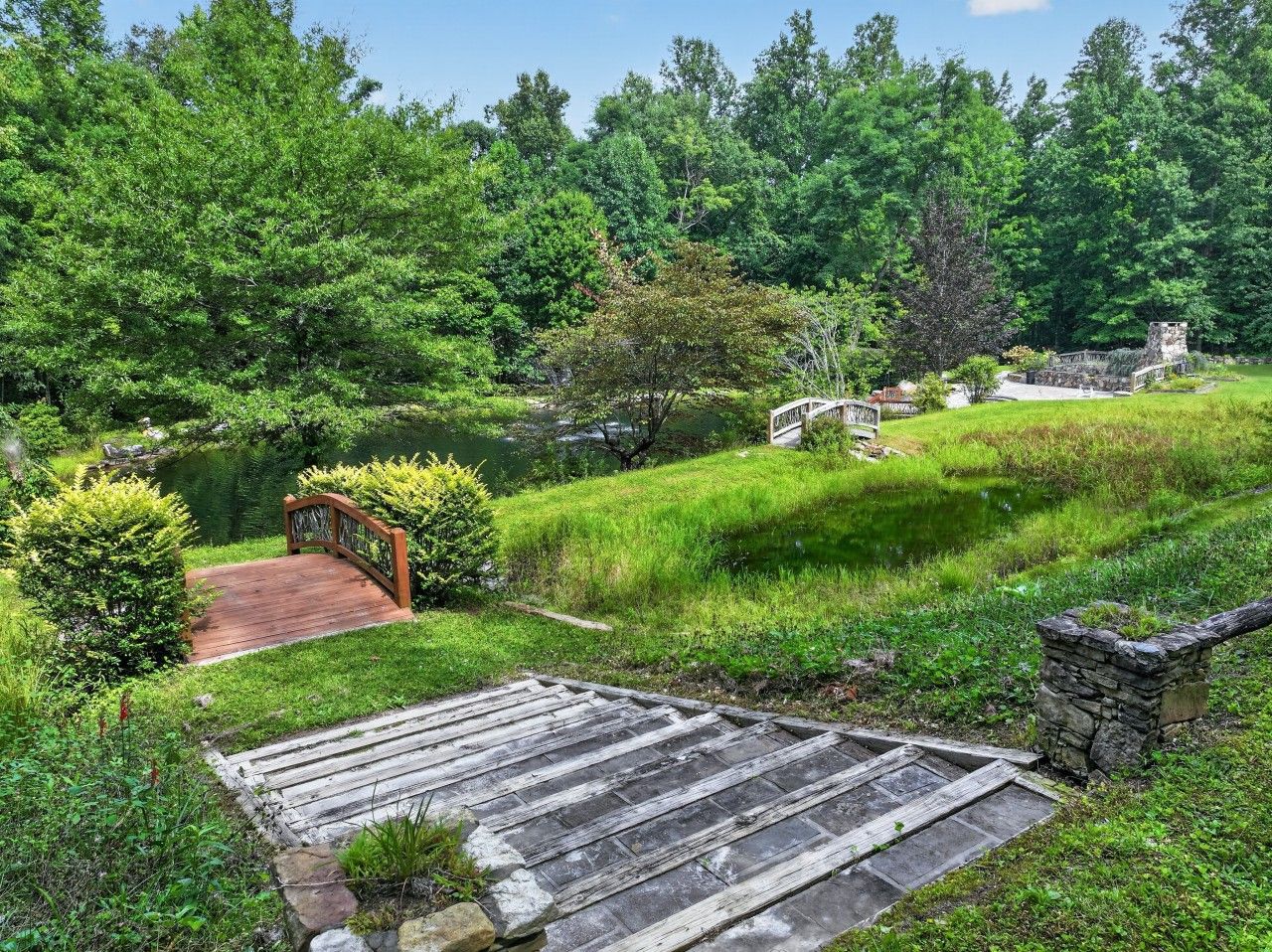 Ein Garten mit einer Holzbrücke, Steinarchitektur und üppigem Grün.
