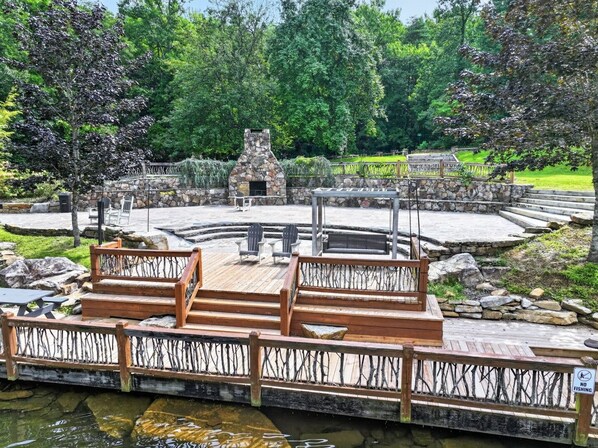 Een openluchttheater van steen, met een stenen podium en zitgedeelte, omgeven door een houten terras en een stenen muur.