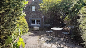 A stone building with a window, a satellite dish, and a table with chairs in a garden area.