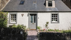 Ein zweistöckiges Haus mit einer grauen Tür, zwei Fenstern im Erdgeschoss und einem kleinen Dachfenster.