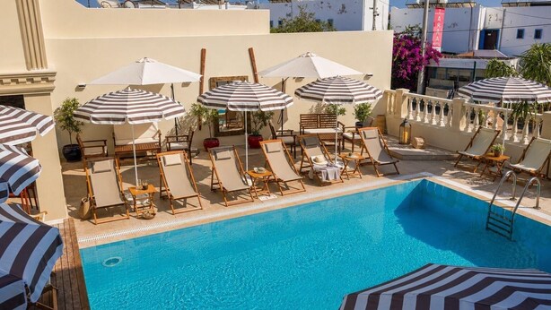 A poolside area with lounge chairs and striped umbrellas, a clear blue pool, and a building with a sign that reads 'IARA HOTEL'. - Ciello Hotel (Bodrum)