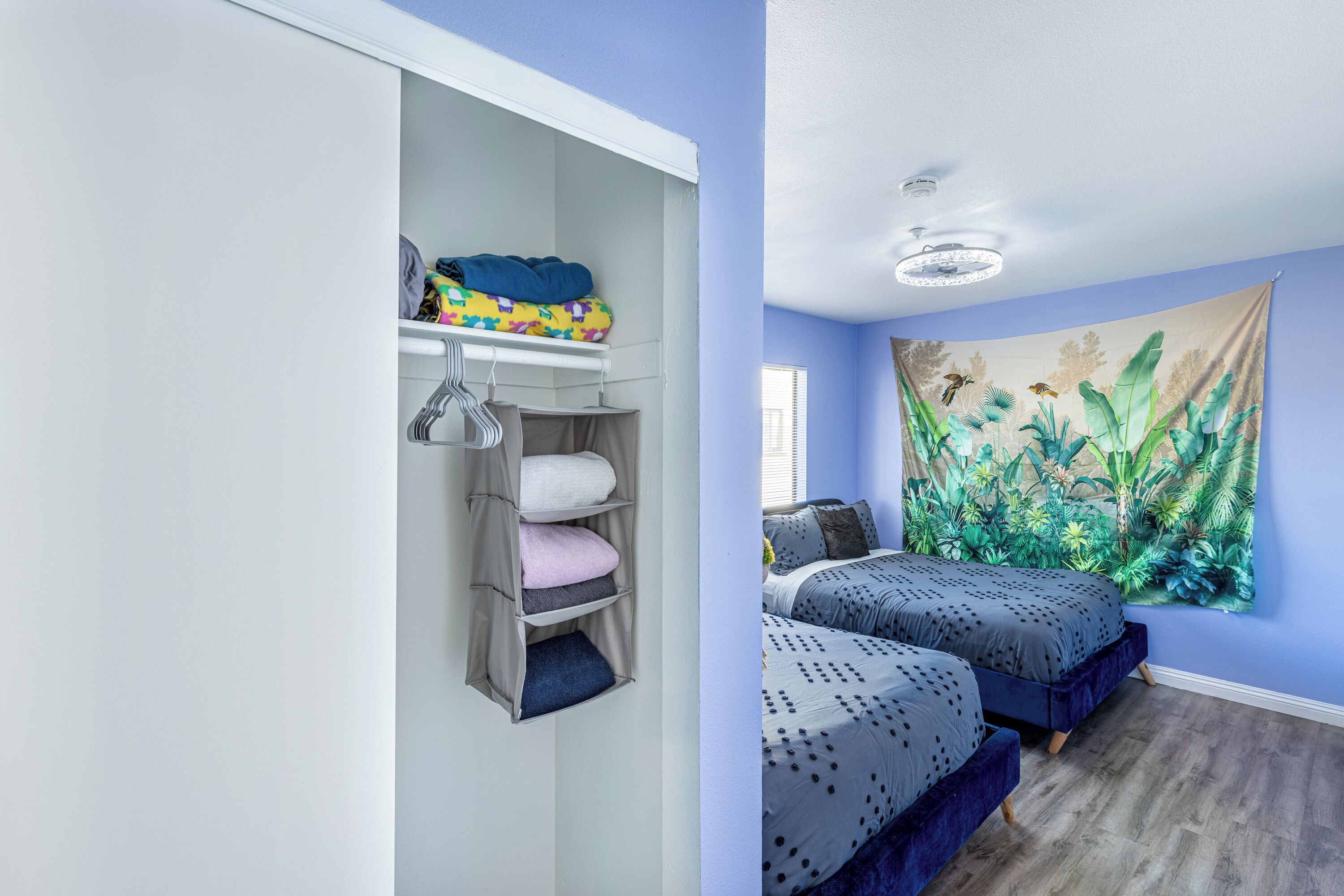 A bedroom with two beds, a closet with shelves, and a large jungle-themed tapestry on the wall.