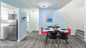 Een moderne keuken met een roestvrijstalen koelkast, een eethoek met een witte tafel en zwarte stoelen, en een trap naar een ander niveau.
