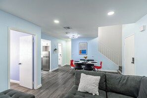 Una sala de estar moderna con un sofá gris, un cojín blanco y una zona de comedor con una mesa y sillas.