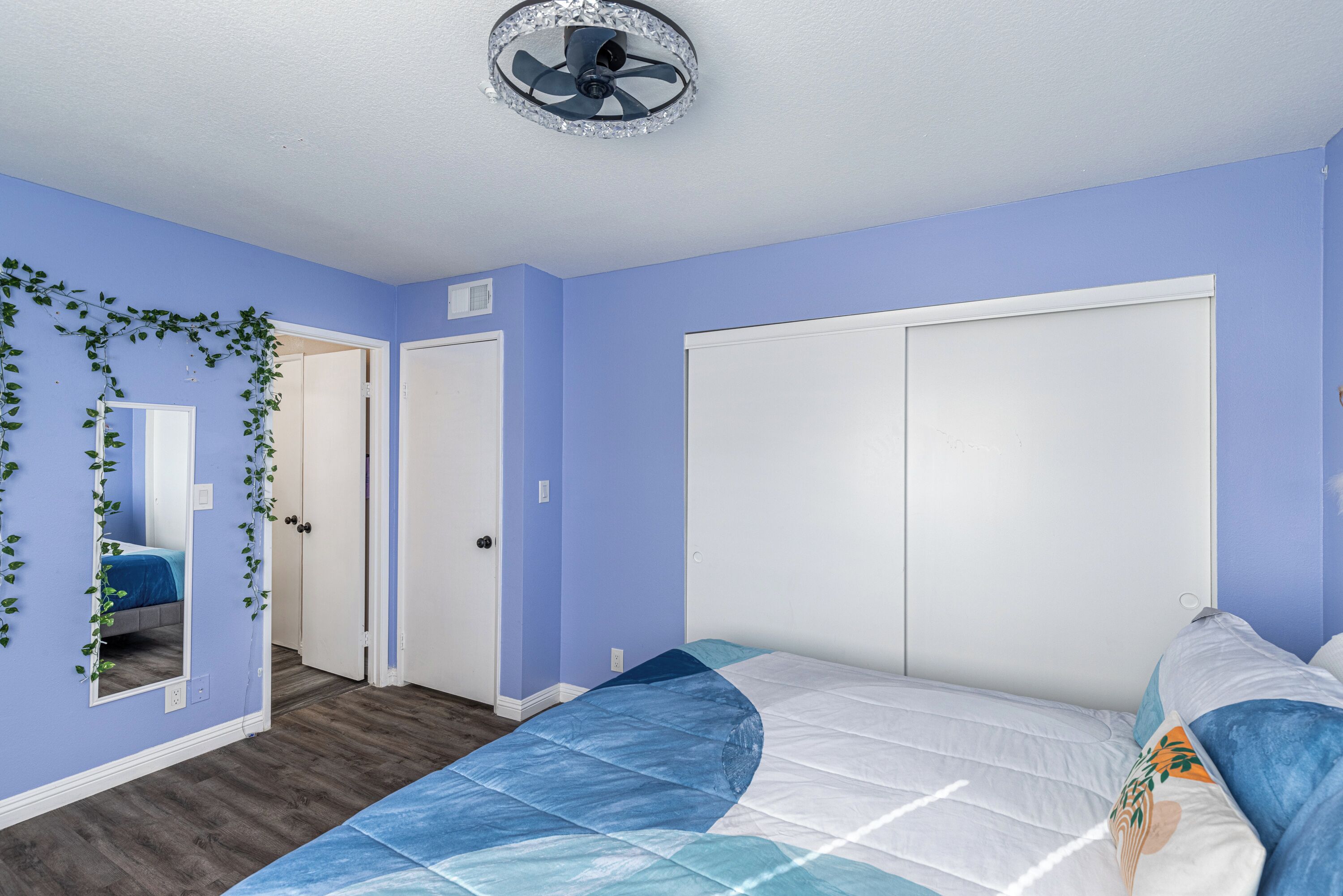 Een slaapkamer met een bed, plafondventilator en een deur.