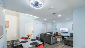 Een moderne woonkamer met een grijze bank, rode stoelen, een eettafel met een wit marmeren blad en een plafondventilator.