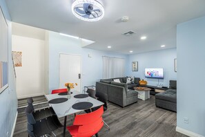 Ein modernes Wohnzimmer mit einem grauen Sofa, roten Sesseln, einem Esstisch mit weißer Marmorplatte und einem Deckenventilator.