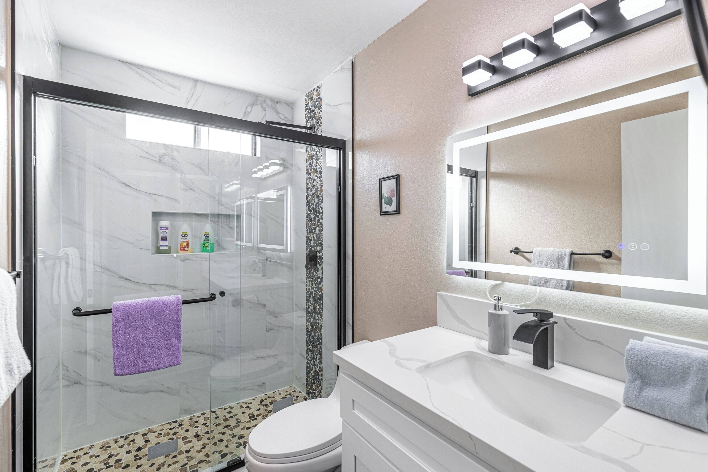 A modern bathroom with a glass shower enclosure, a white sink, and a large mirror.
