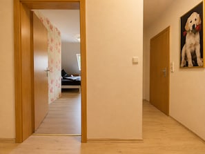 A hallway with wooden flooring, a door leading to a bedroom with a bed, and a painting of a dog on the wall. - Cozy Attic Apartment (Boppard)