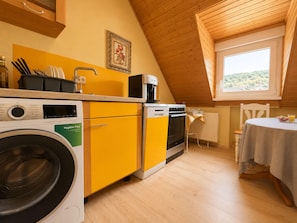 A kitchen with a washing machine, a coffee maker, and a dining area with a table. - Cozy Attic Apartment (Boppard)