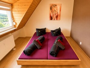 A room with a sloped ceiling, a bed with purple bedding, two black pillows, and a painting on the wall. - Cozy Attic Apartment (Boppard)