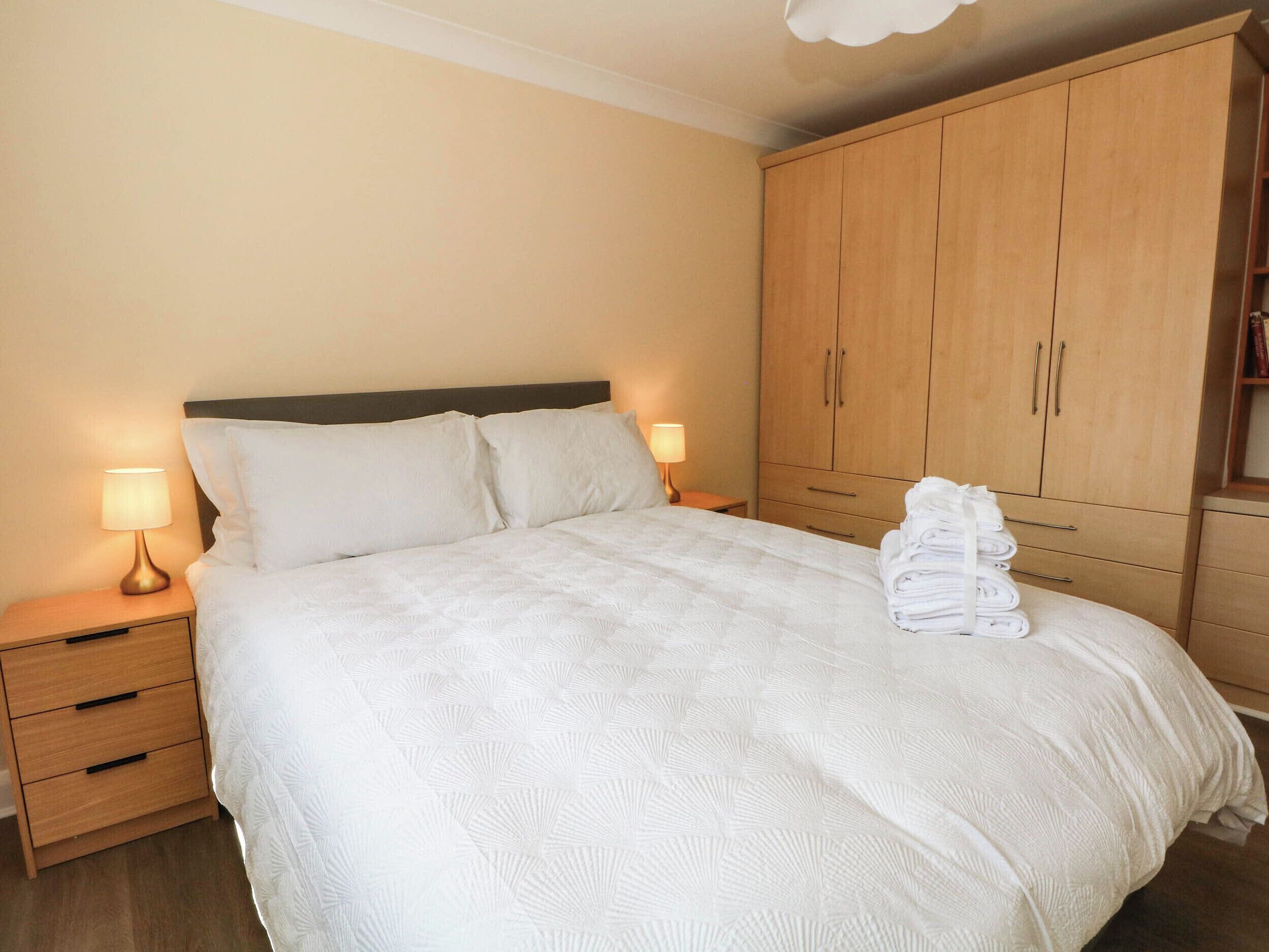 Ein Hotelzimmer mit Bett, Nachttischen, einem Kleiderschrank und einem ordentlich gefalteten Handtuch auf dem Bett.