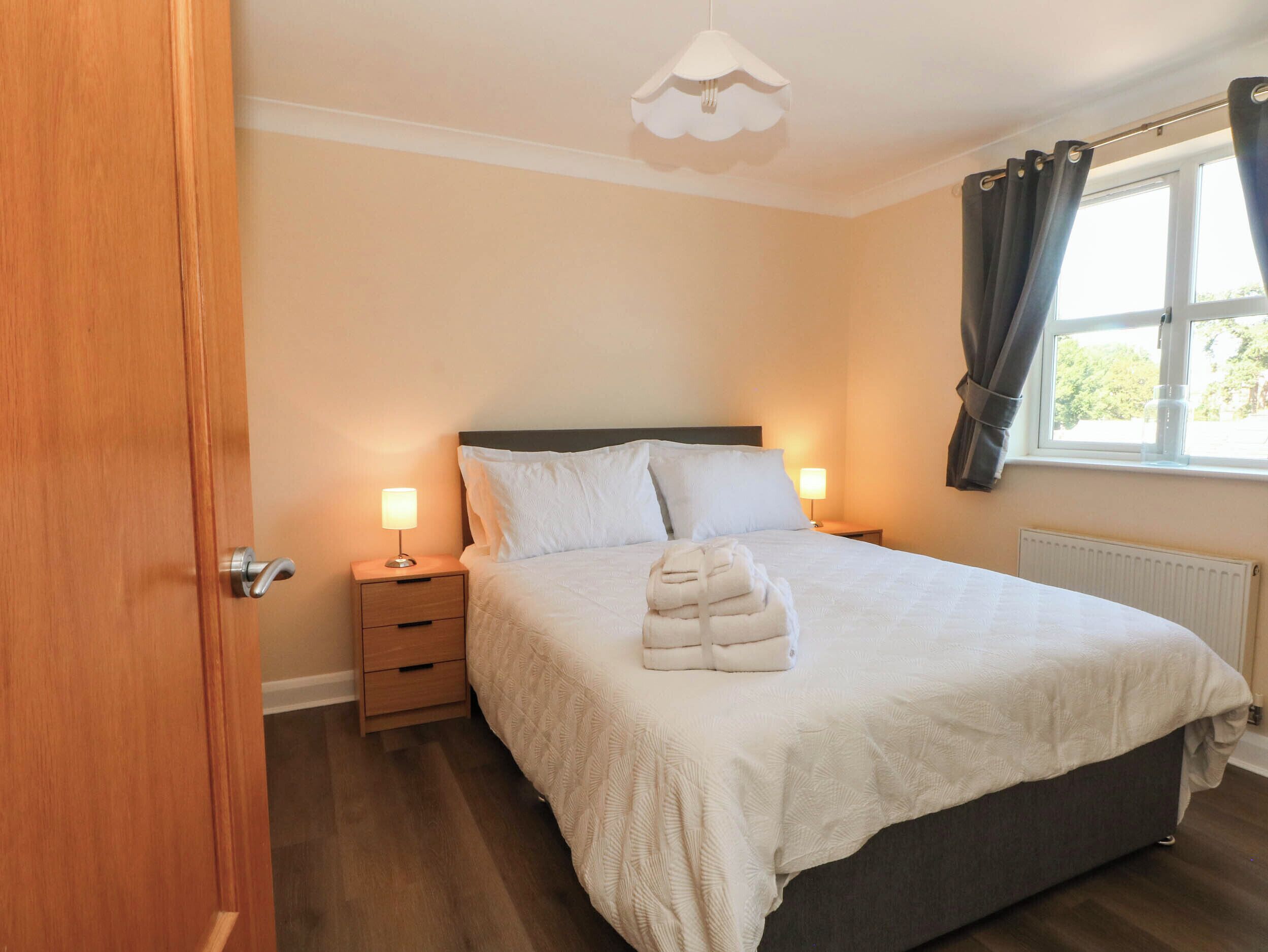 A bedroom with a bed, bedside lamps, a nightstand, a window with curtains, and a door.
