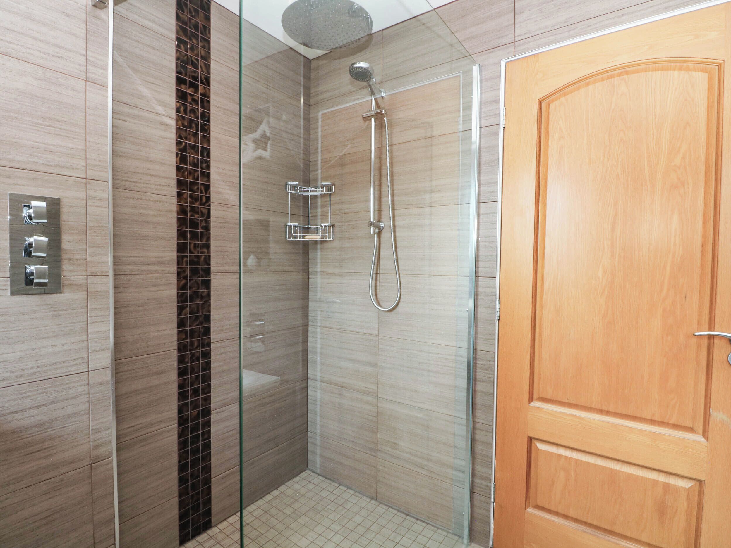 Une salle de bain moderne avec une douche à parois de verre, une porte en bois et un sol carrelé.