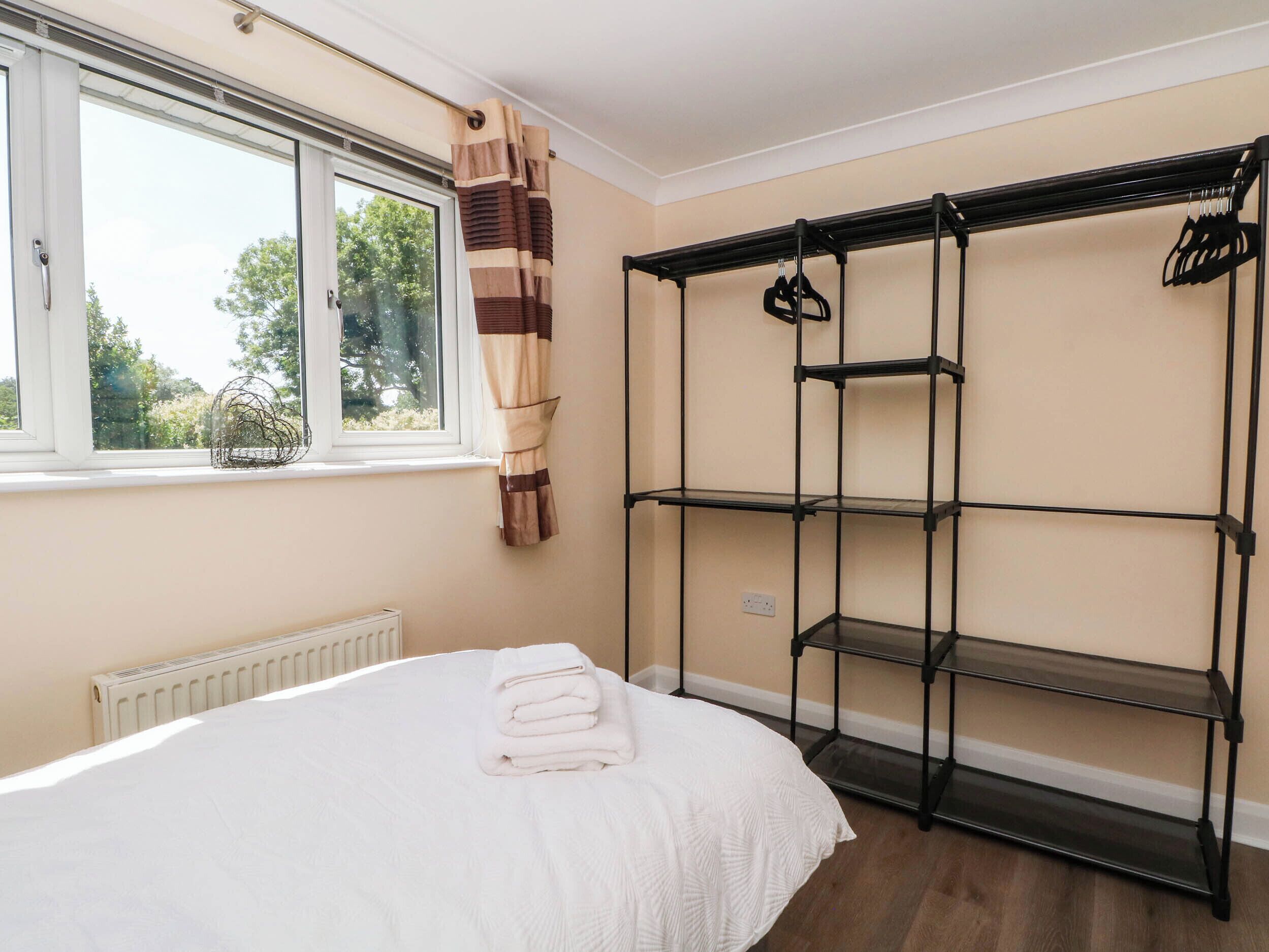 Een slaapkamer met een bed, een raam, een radiator en een zwarte metalen plankkast.