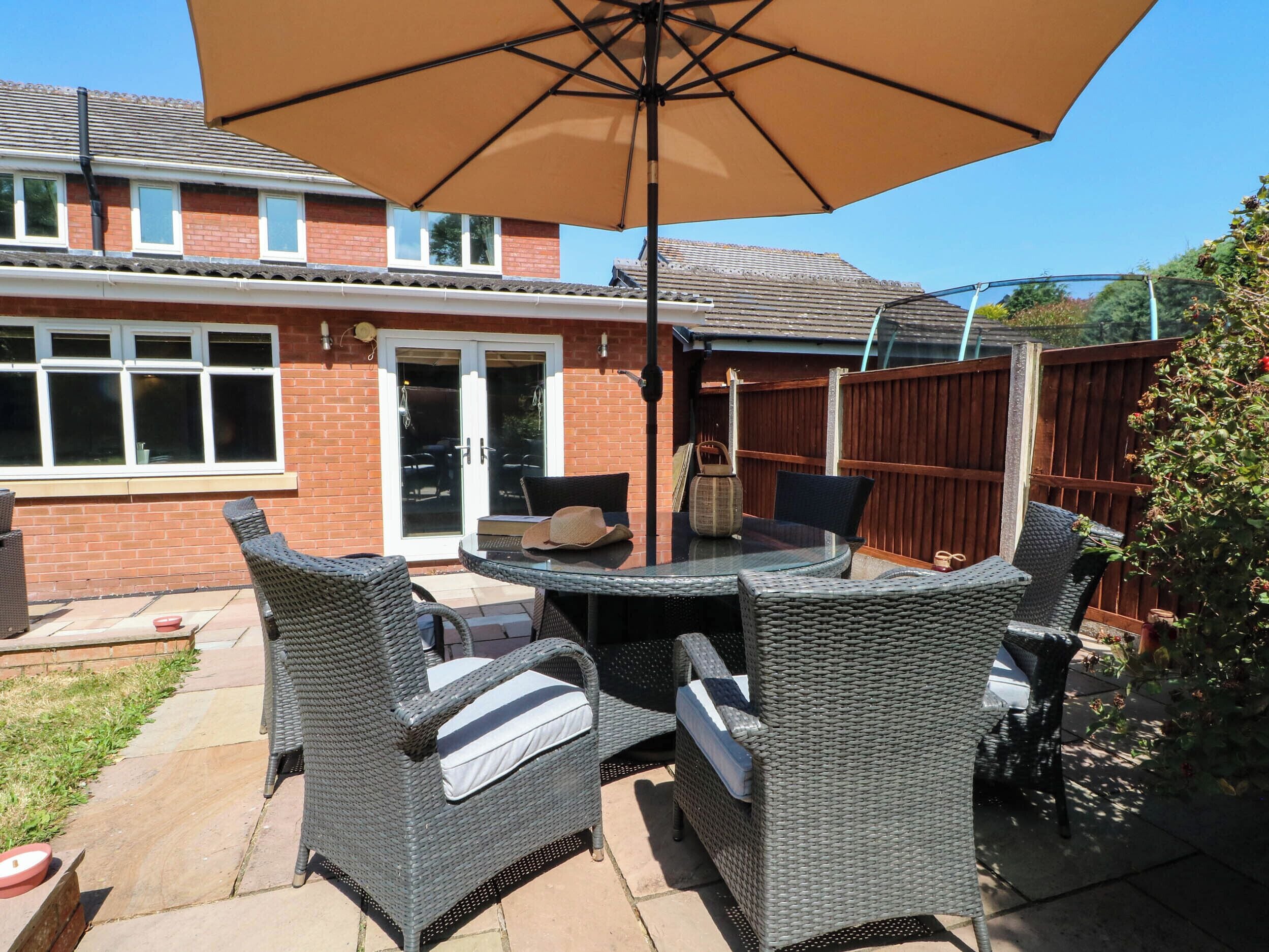 An outdoor patio with wicker furniture, a glass table, and a brown umbrella.