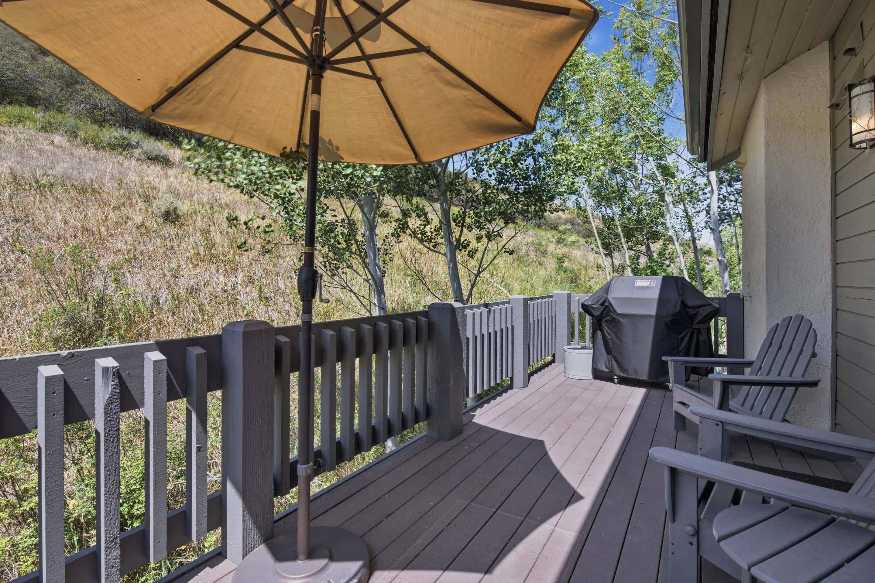 A deck with a grill, chairs, and a large umbrella.