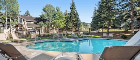 A pool area with lounge chairs, a small table, and a fenced pool.