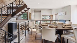 A modern dining area with a round table, white chairs, and a wooden staircase. - Ridgepoint Townhome 166 - 4 Bedroom Residence (Beaver Creek)