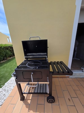 A portable grill with wheels, positioned on a tiled patio.