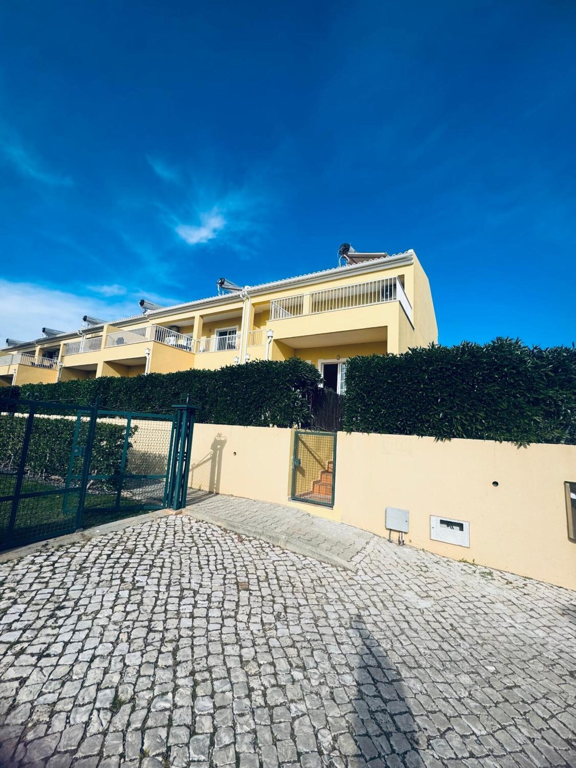 A multi-story building with a yellow facade, a paved courtyard, and a green gate.
