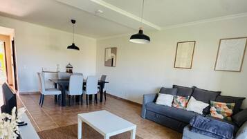 A living room with a sofa, a coffee table, and a dining area with chairs and a table.